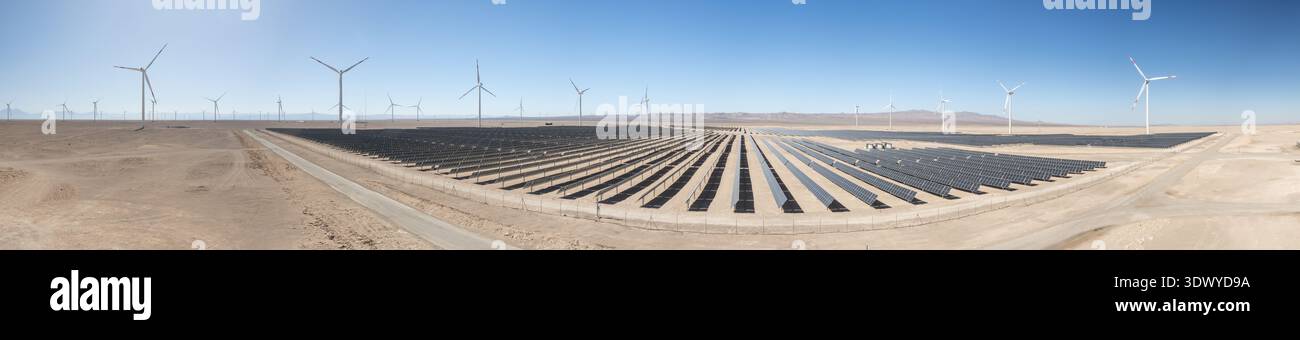 Plan grand angle d'un panneau solaire à grande échelle avec des éoliennes en arrière-plan sous un ciel bleu clair Banque D'Images