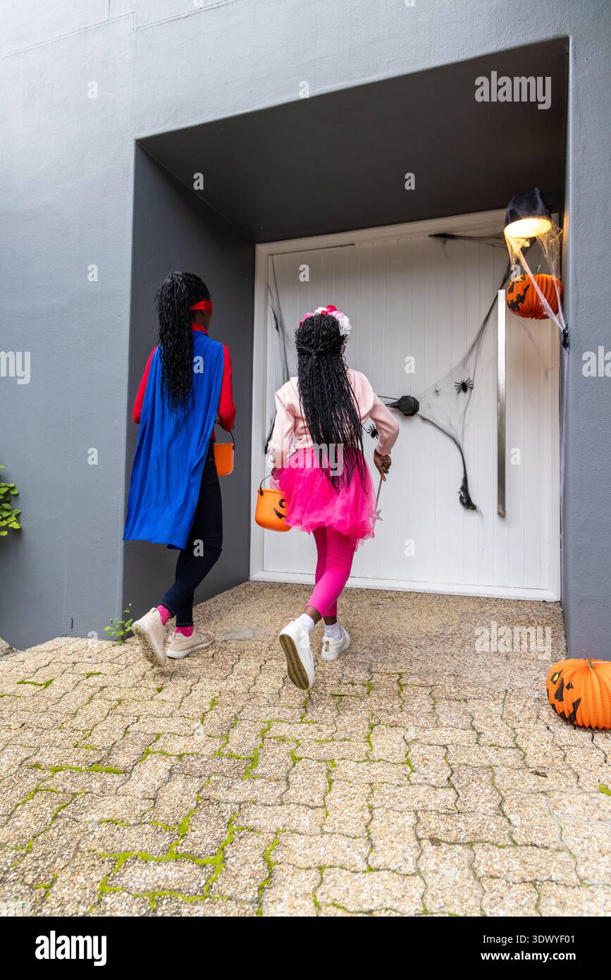Deux filles afro-américaines 6-10 Trick-or-Treatment à la porte avec de fausses toiles et des seaux de citrouille orange Banque D'Images