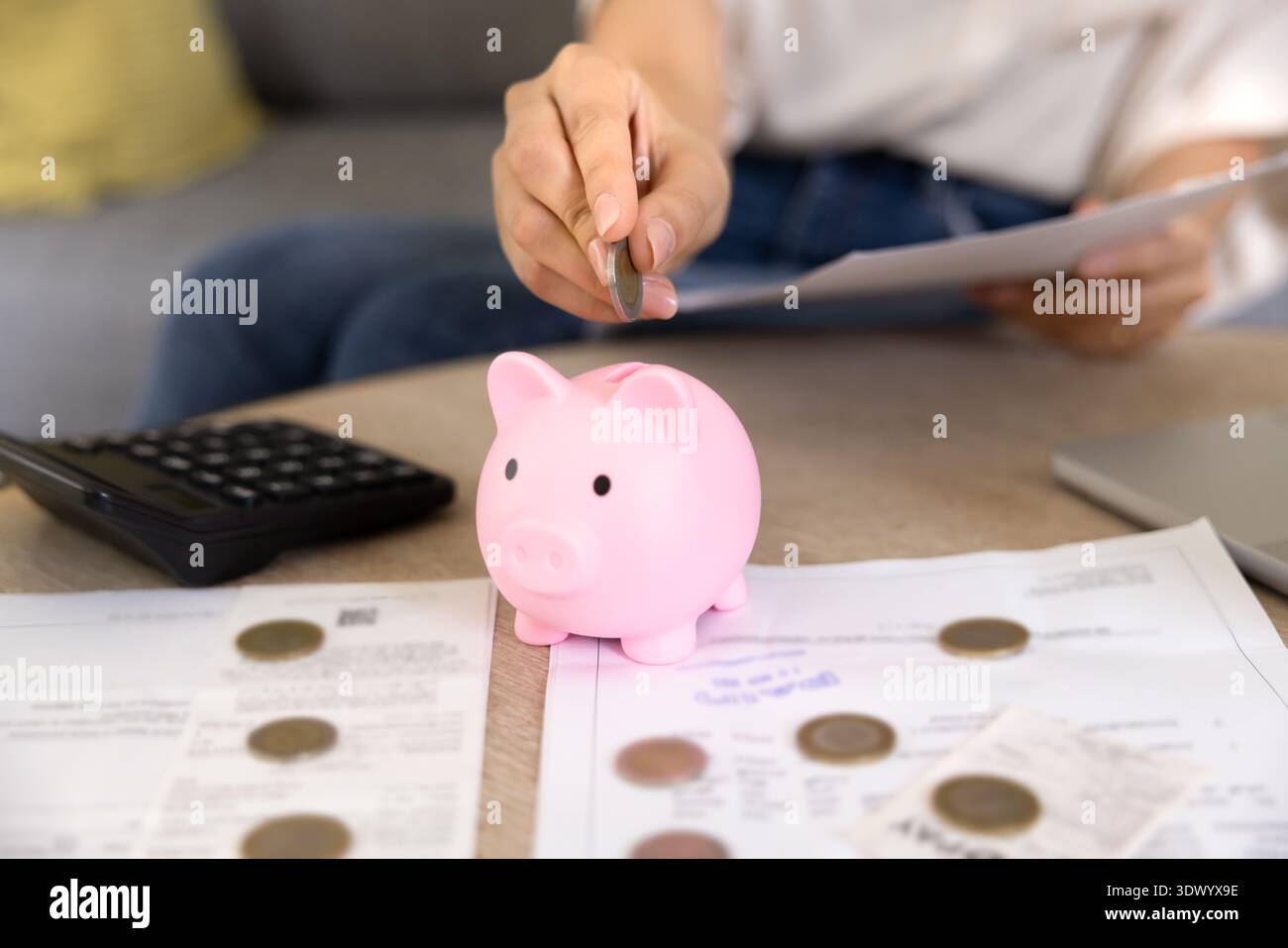 Jeune femme qui dépose des pièces dans une tirelire Banque D'Images