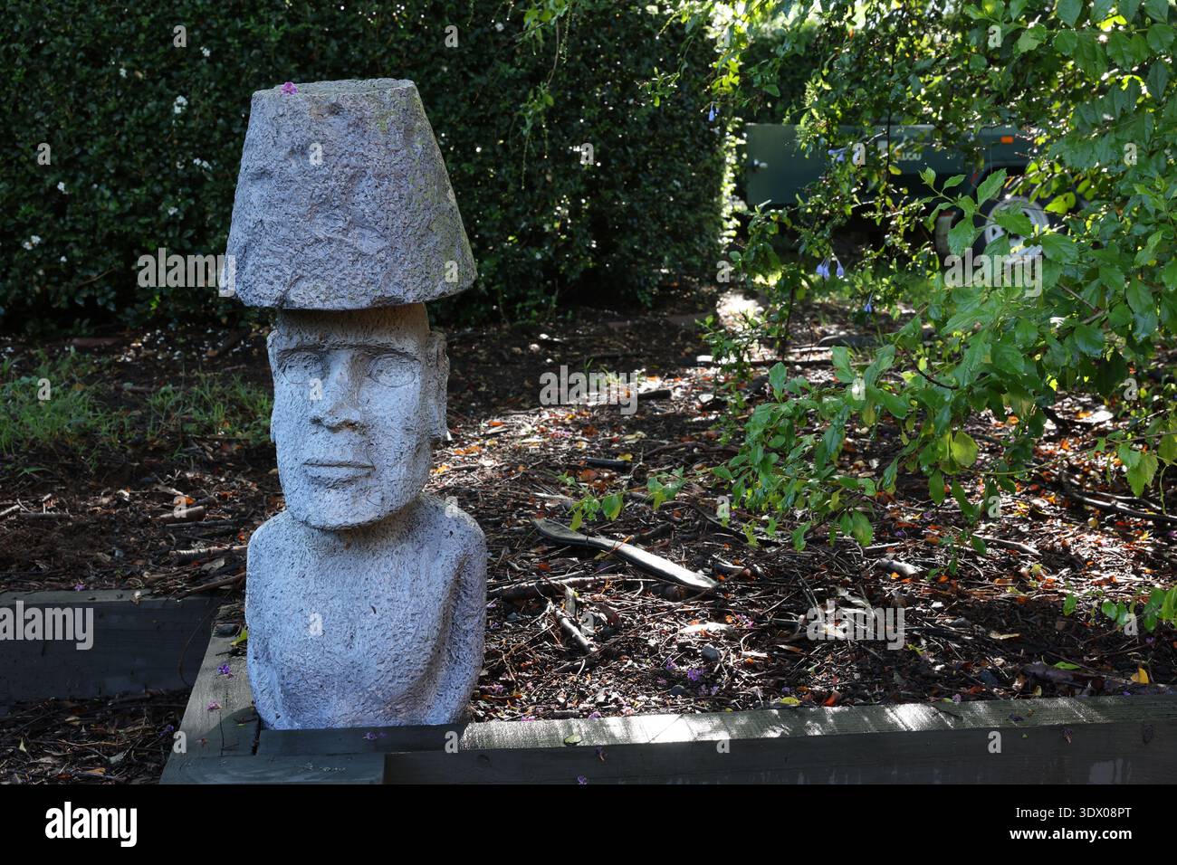 Statue de jardin en pierre avec visage humain et chapeau dans un cadre paysager extérieur. Banque D'Images