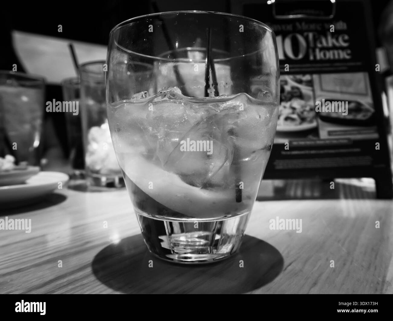 Verre d'eau glacée sur la table du restaurant avec menu flou en arrière-plan, photographie en noir et blanc Banque D'Images
