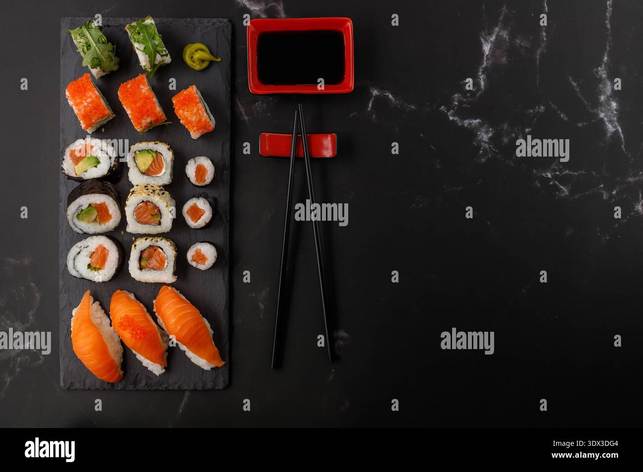 Délicieux ensemble de sushis assortis avec baguettes et sauce soja sur planche de pierre. Sushi maki avec masago, caviar, avocat, sésame, saumon, roquette. Sombre Banque D'Images