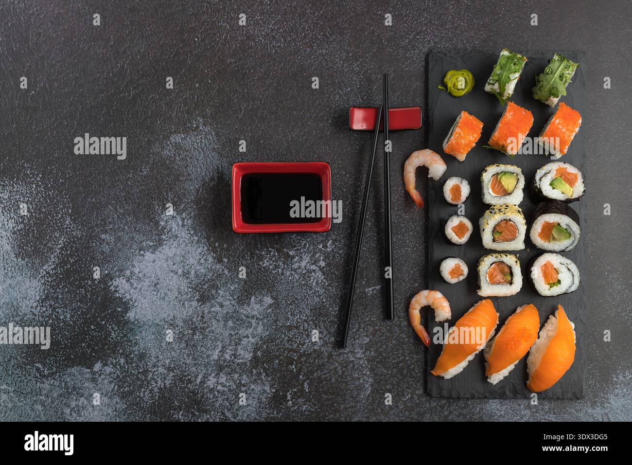 Délicieux ensemble de sushis assortis avec baguettes et sauce soja sur planche de pierre. Sushi maki avec masago, caviar, avocat, sésame, saumon, roquette. Sombre Banque D'Images