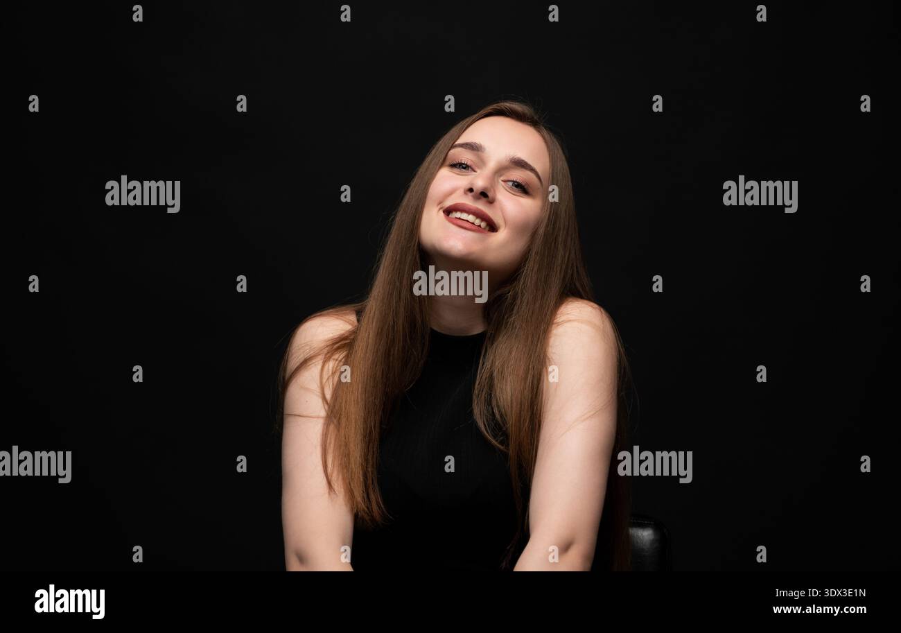 Jeune femme souriant avec un large sourire, se sentant heureuse et joyeuse, posant en studio avec un fond noir, regardant la caméra Banque D'Images