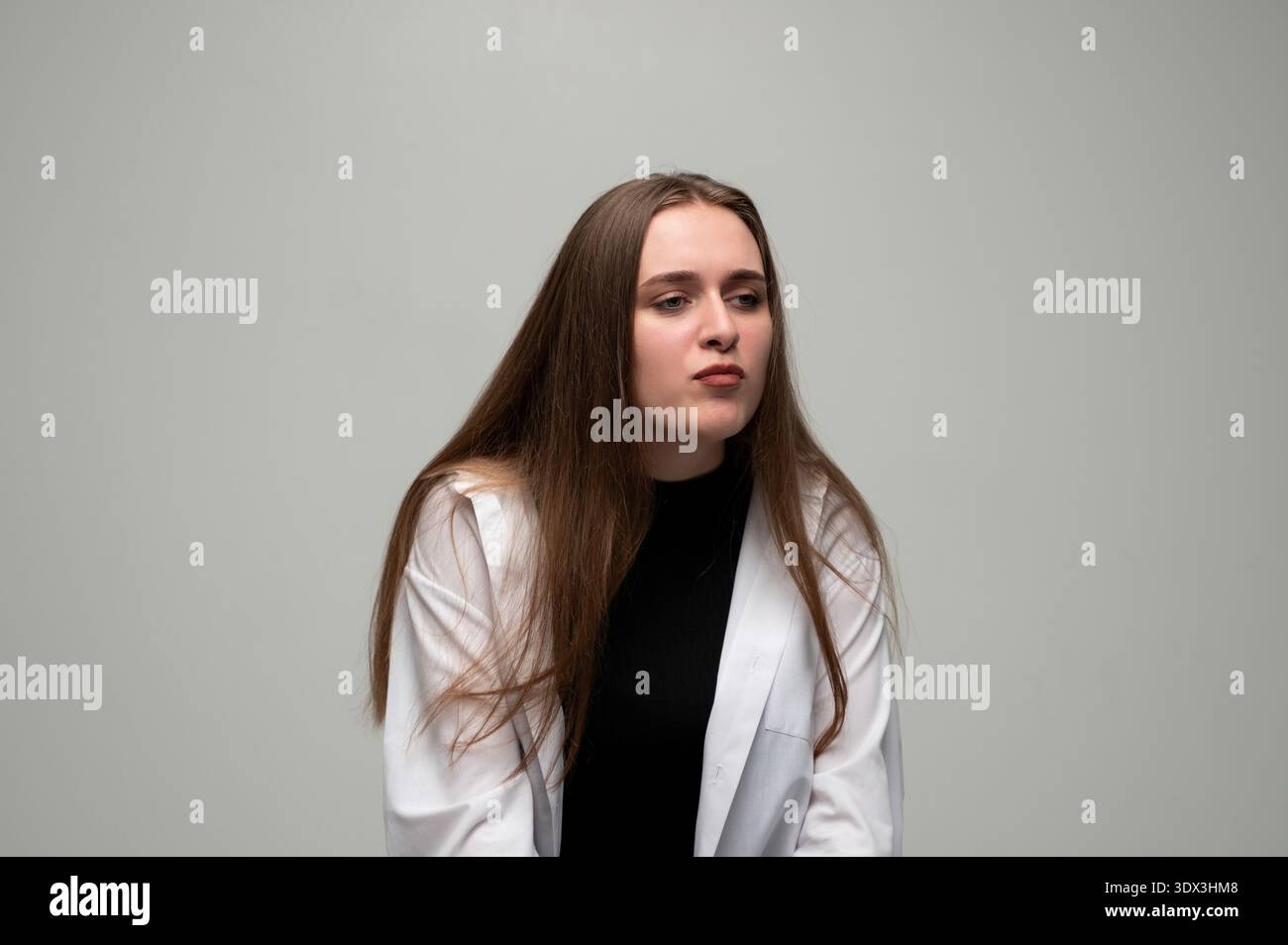 Jeune femme avec de longs cheveux regardant loin, exprimant le doute et l'incertitude sur un fond Uni Banque D'Images