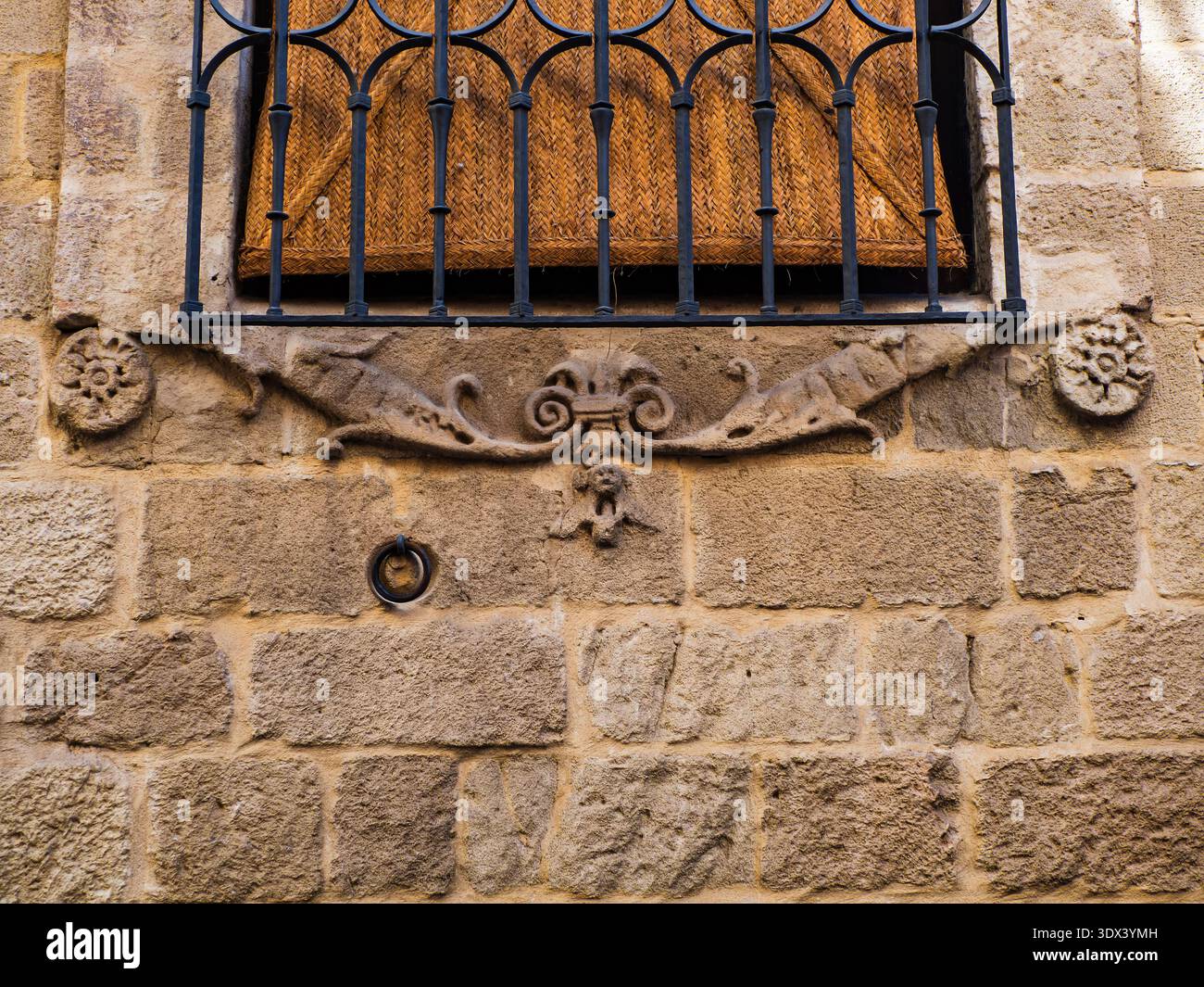 Un détail architectural historique, d'une fenêtre avec une grille en fer forgé et un épais rideau de paille monté sur une façade en pierre. Banque D'Images