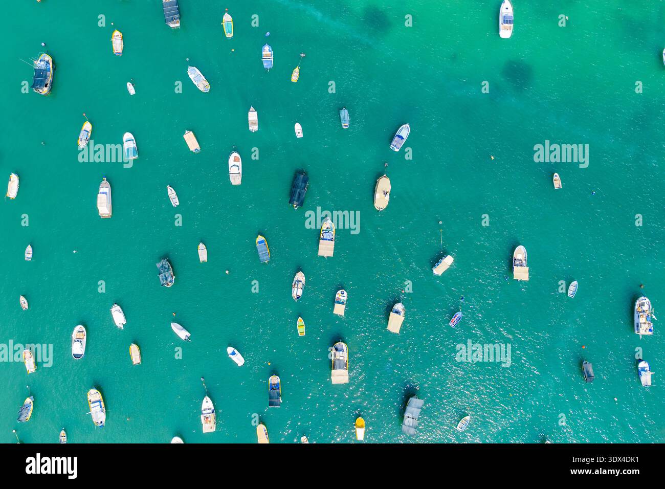 Vue aérienne de haut en bas de petits bateaux ancrés dans une eau turquoise claire à la marina de Marsaxlokk, Malte, avec des points d'amarrage dispersés et des surfa de mer ondulés Banque D'Images
