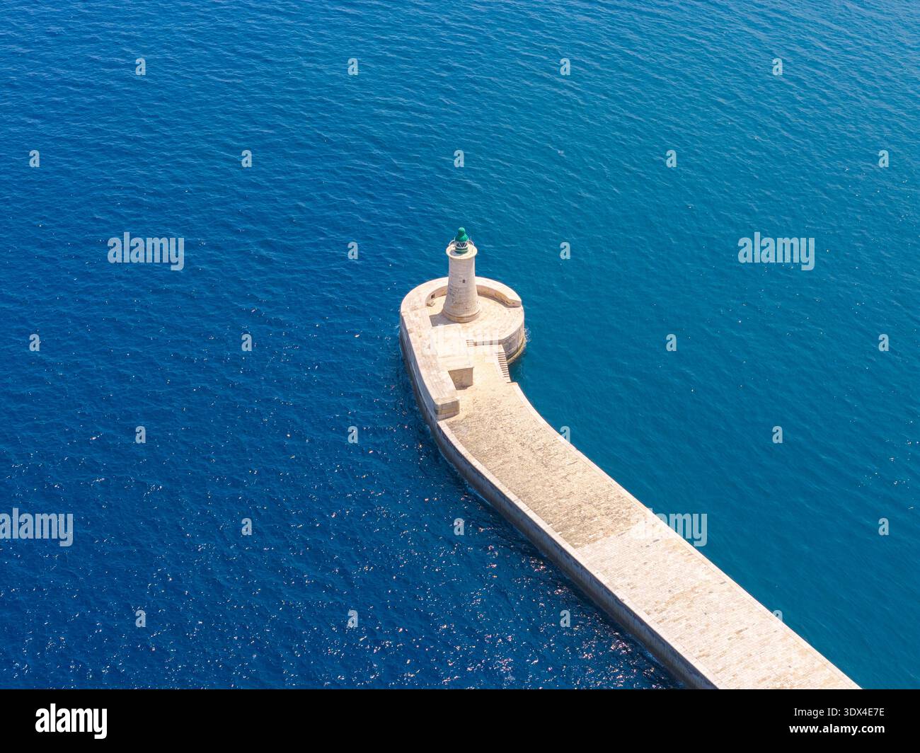 Vue aérienne du brise-lames Ricasoli East à Kalkara, Malte, avec phare à la pointe et texture bleu profond de la mer Méditerranée. Banque D'Images