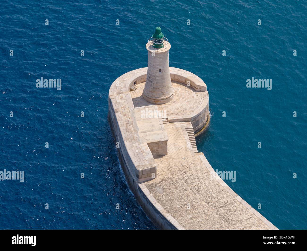 Vue aérienne de la pierre courbée Ricasoli East Breakwater avec un petit phare, projetant dans la mer Méditerranée bleu profond près de Kalkara, Malte. Banque D'Images