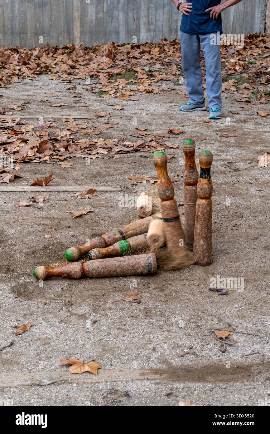 Vue en angle élevé des épingles en bois traditionnelles tombant pendant un jeu de Bitlles sur une surface de terre. Concept : action, succès et réalisation des objectifs. Banque D'Images