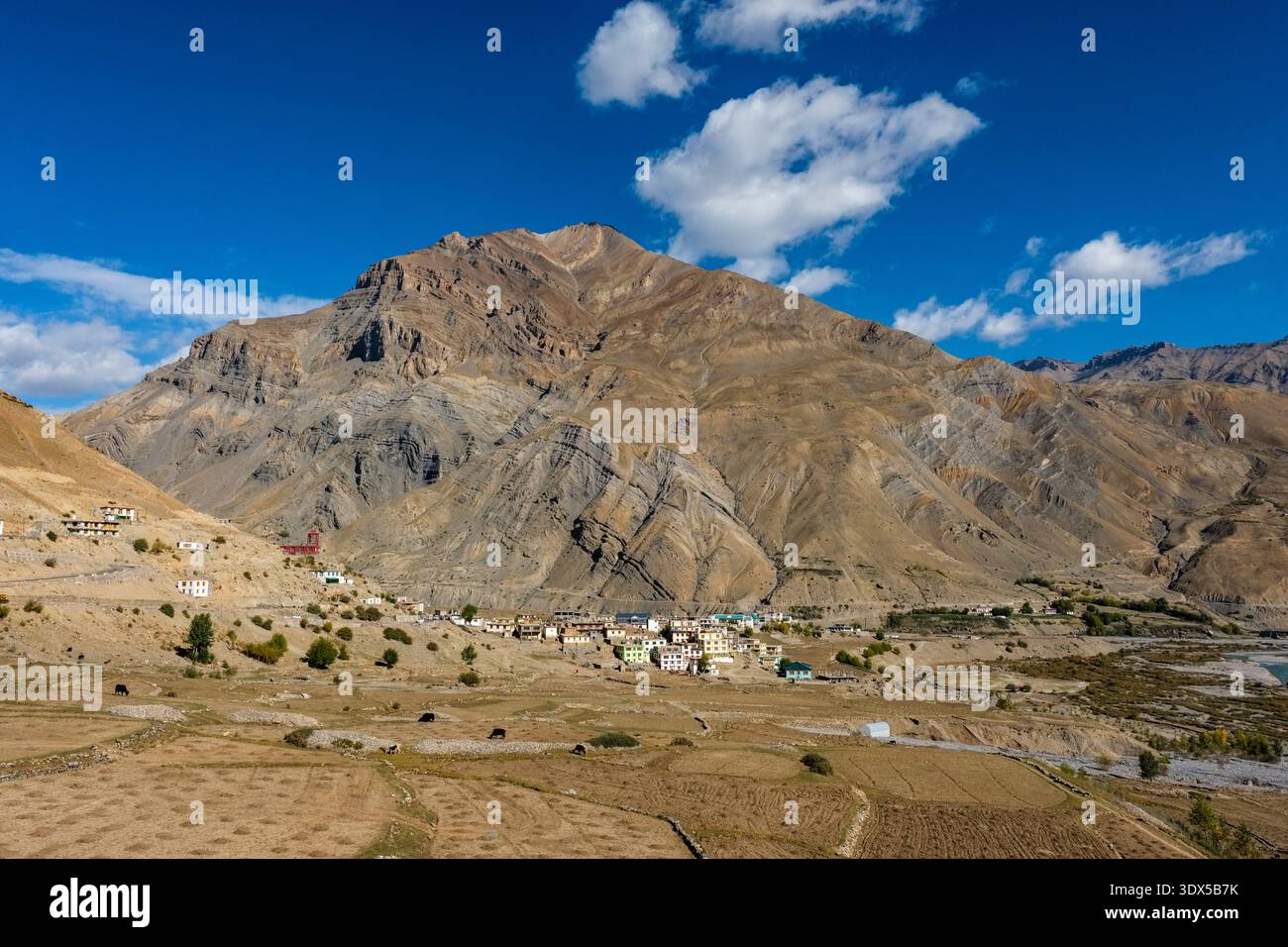 Village de Sagnam avec des maisons traditionnelles et des champs en terrasses au-dessous d'une crête de montagne escarpée sous un ciel bleu avec des nuages dispersés. Banque D'Images
