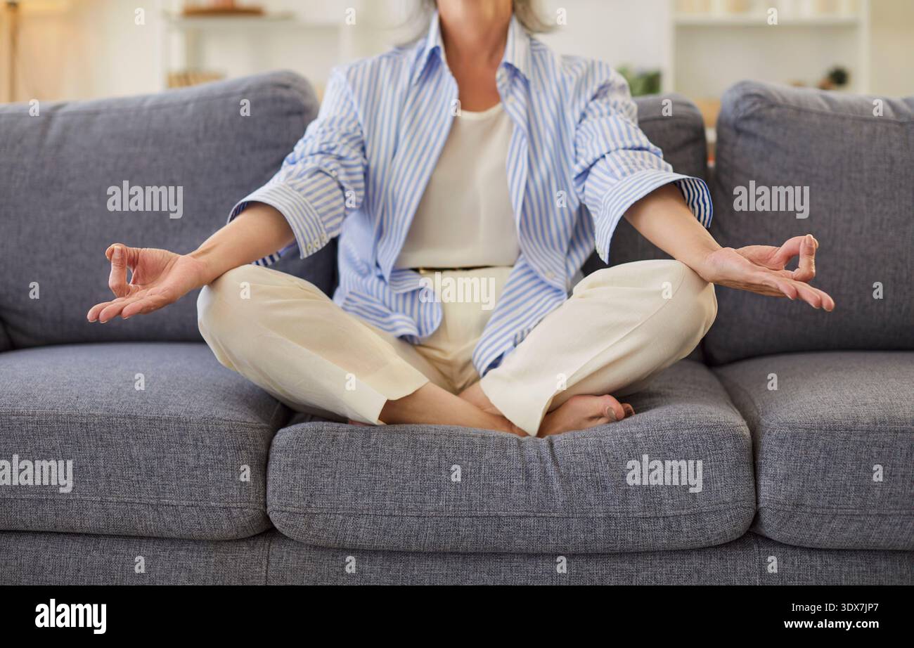 Senior consciente femme mature saine assise dans la pose de lotus pratiquant la méditation à la maison, senior calme Banque D'Images