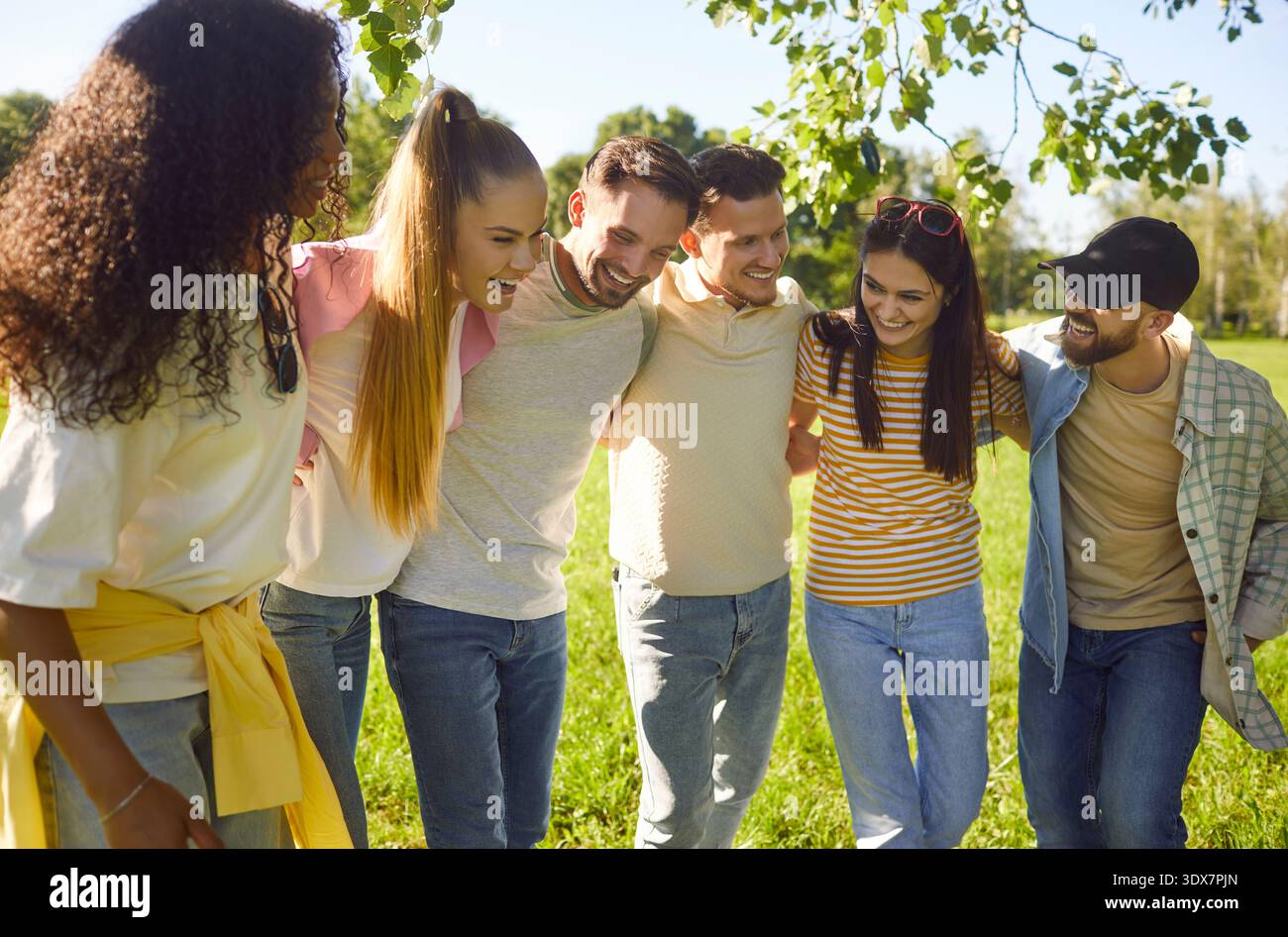 Heureux amis debout étroitement embrassant dans le parc vert d'été ensoleillé, groupe amical diversifié souriant Banque D'Images