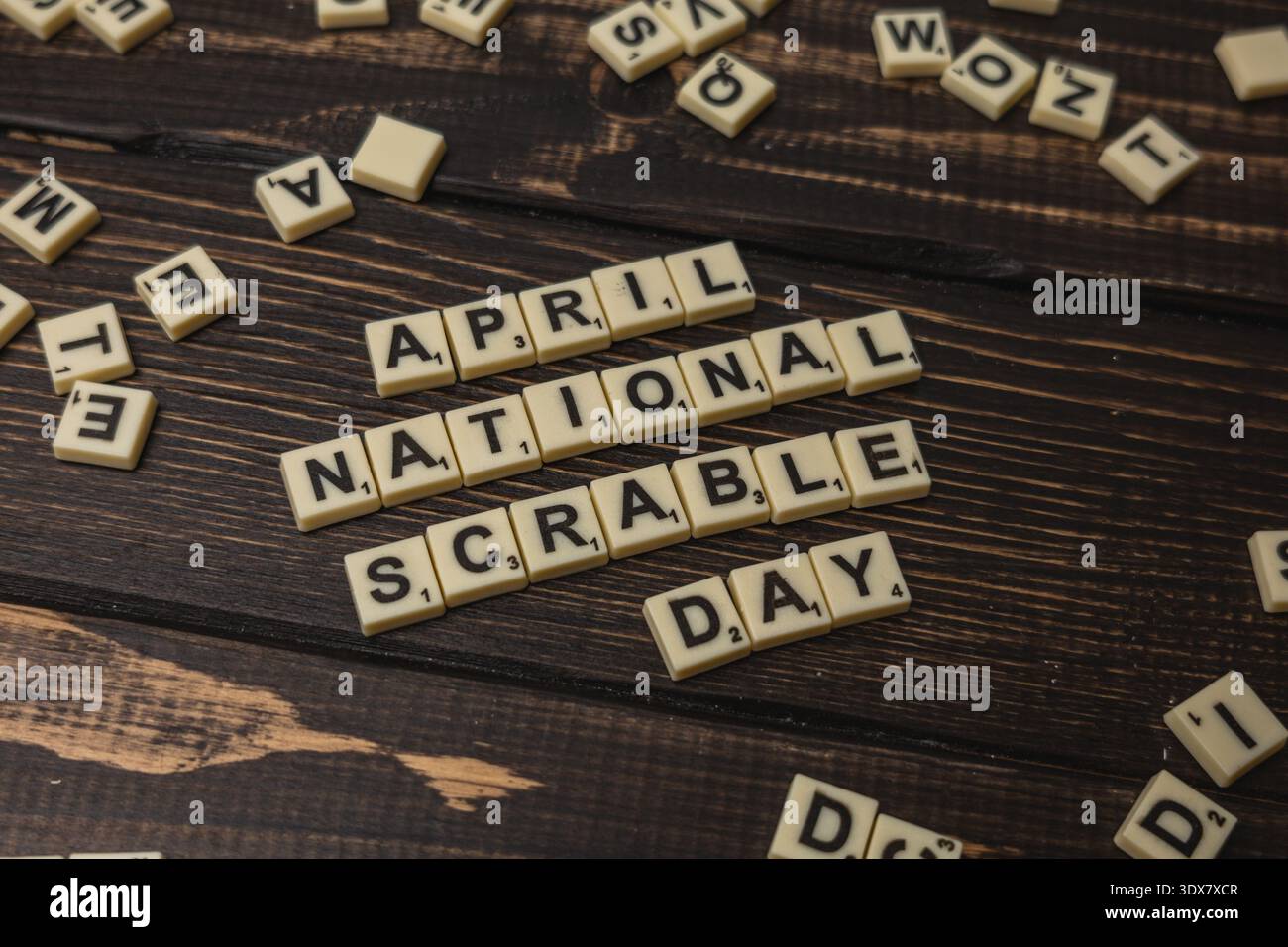 Des lettres dispersées sur une table en bois décrivent la Journée nationale du Scrabble pour que les joueurs puissent en profiter. L'activité se déroule en avril, mettant l'accent sur les jeux de mots et le plaisir Banque D'Images