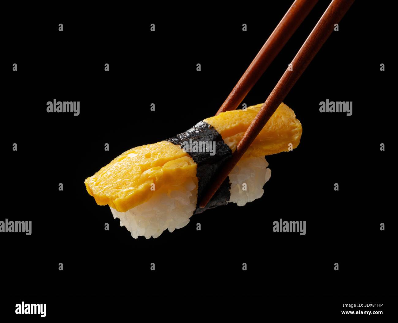 Gros plan de baguettes tenant des sushis tamago oeuf nigiri sur fond noir Banque D'Images
