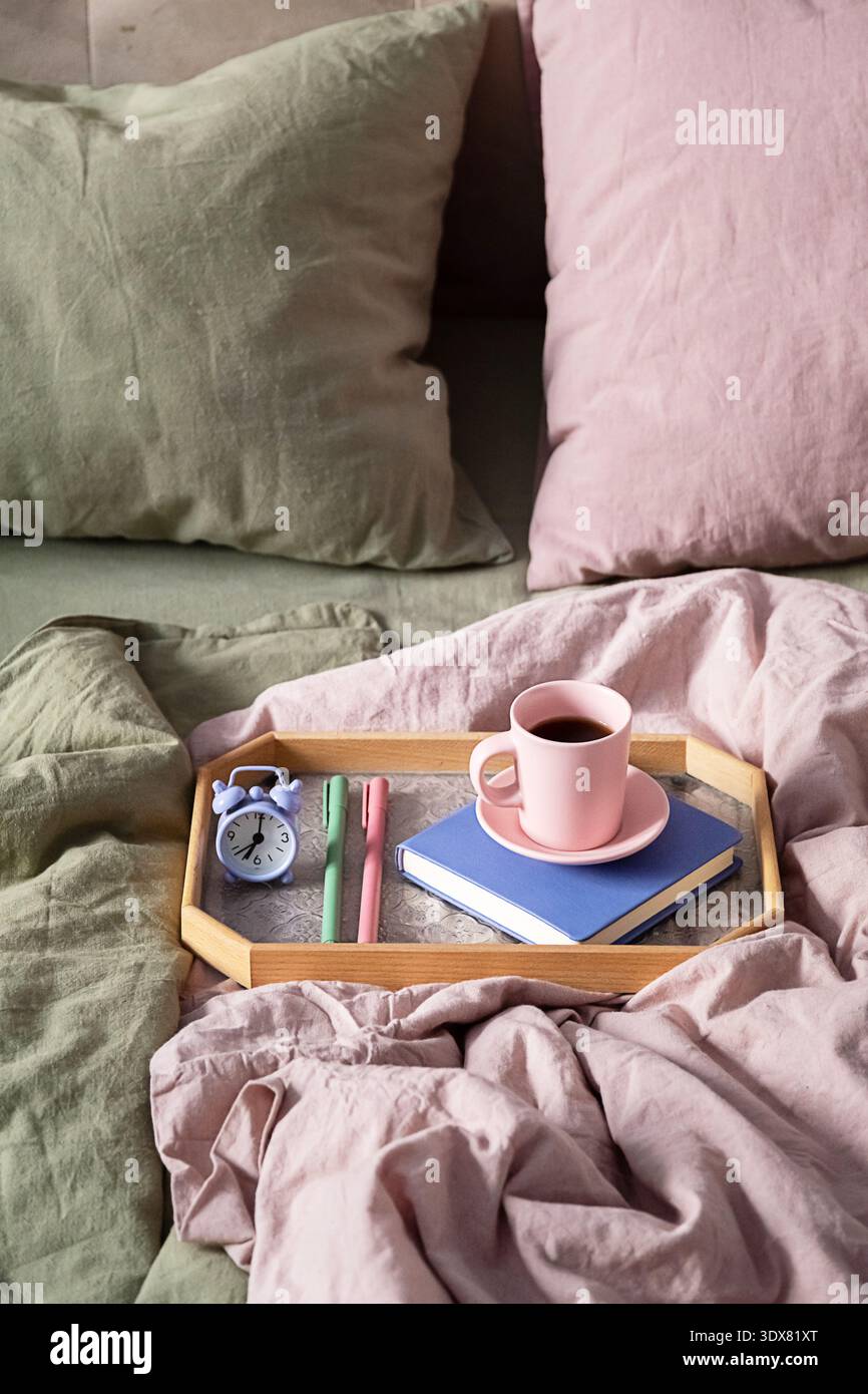Petit déjeuner au lit, plateau en bois avec tasse à café, livre et réveil. Ambiance chaleureuse du matin à la maison. Week-end paresseux relaxant. Banque D'Images