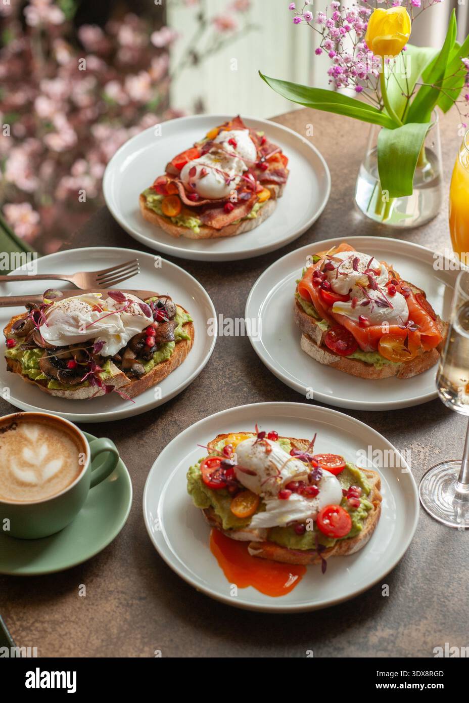 Une table de brunch magnifiquement stylisée avec quatre toasts à l'avocat différents surmontés d'œufs pochés, bacon, champignons, saumon et tomates, accentué avec Banque D'Images