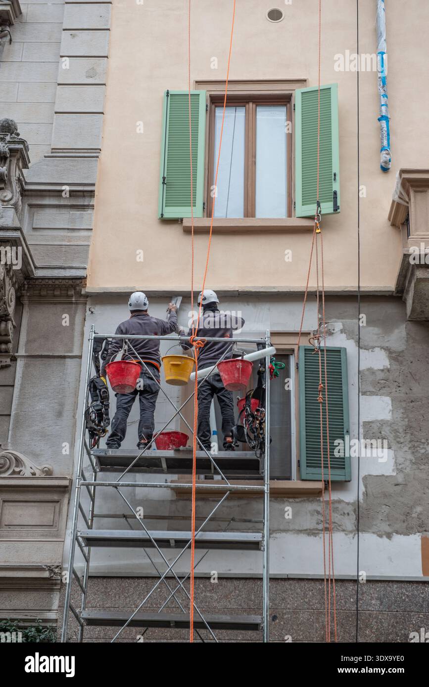 Milan Italie 27 février 2026 : deux ouvriers portant des casques et des équipements de sécurité travaillent sur des échafaudages métalliques lors de travaux de maintenance et de rénovation Banque D'Images