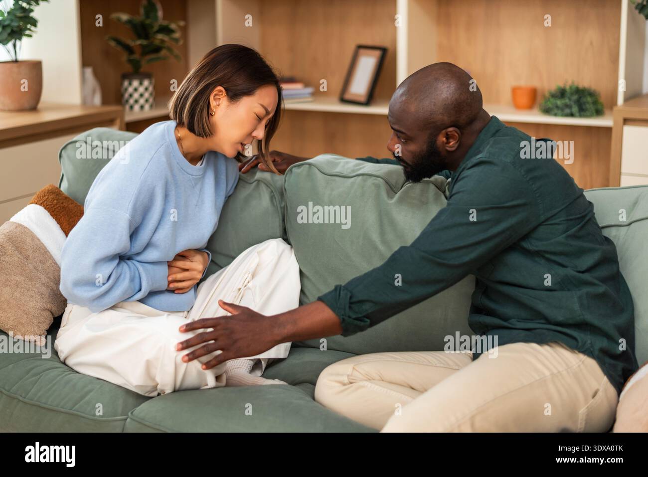 Couple multiracial adulte assis sur le canapé à la maison à parler de leurs problèmes de santé. Banque D'Images