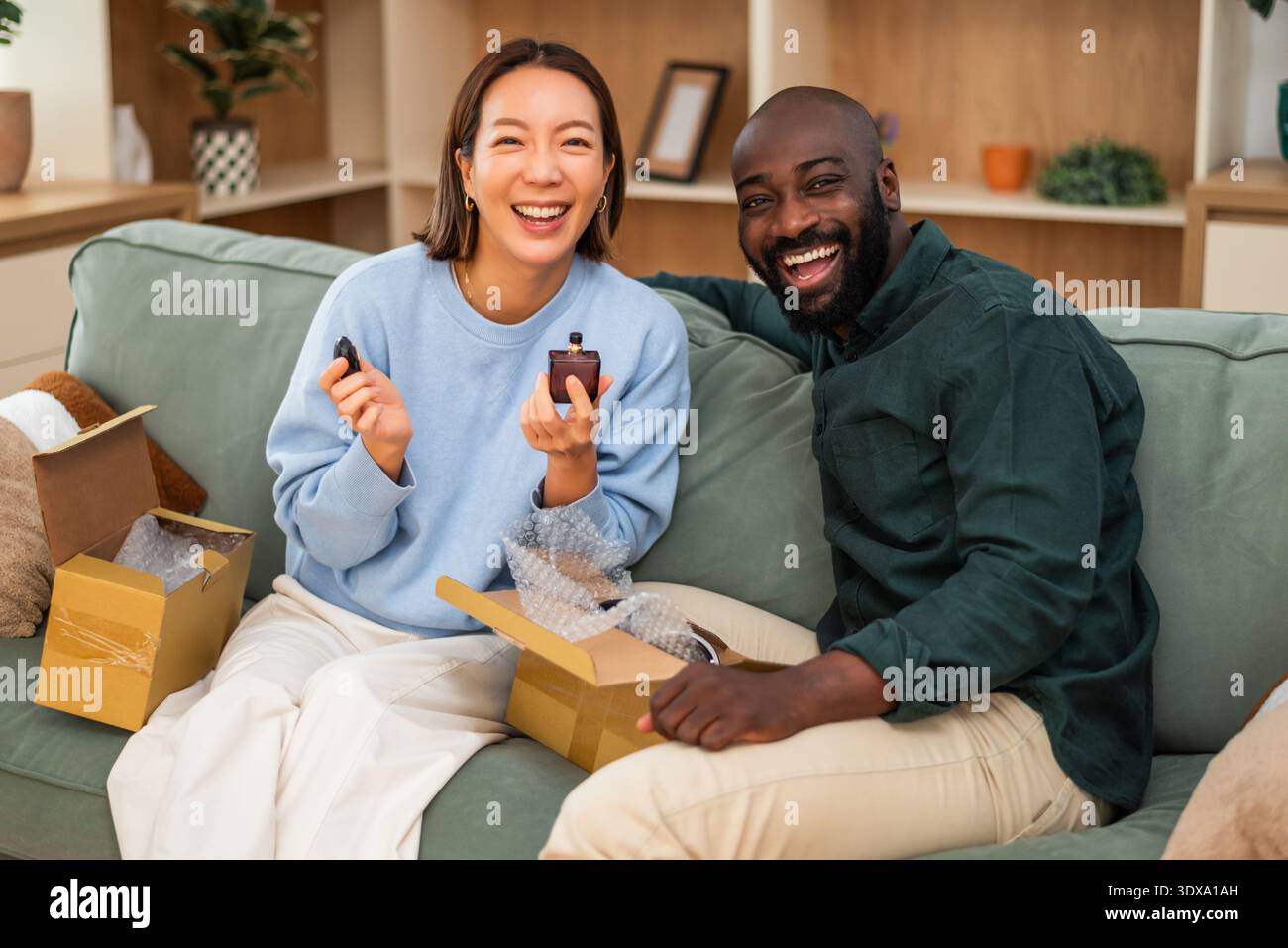 Un couple multiracial se détend sur le canapé, examinant une commande en ligne alors qu'ils déballent un parfum fraîchement livré. Banque D'Images