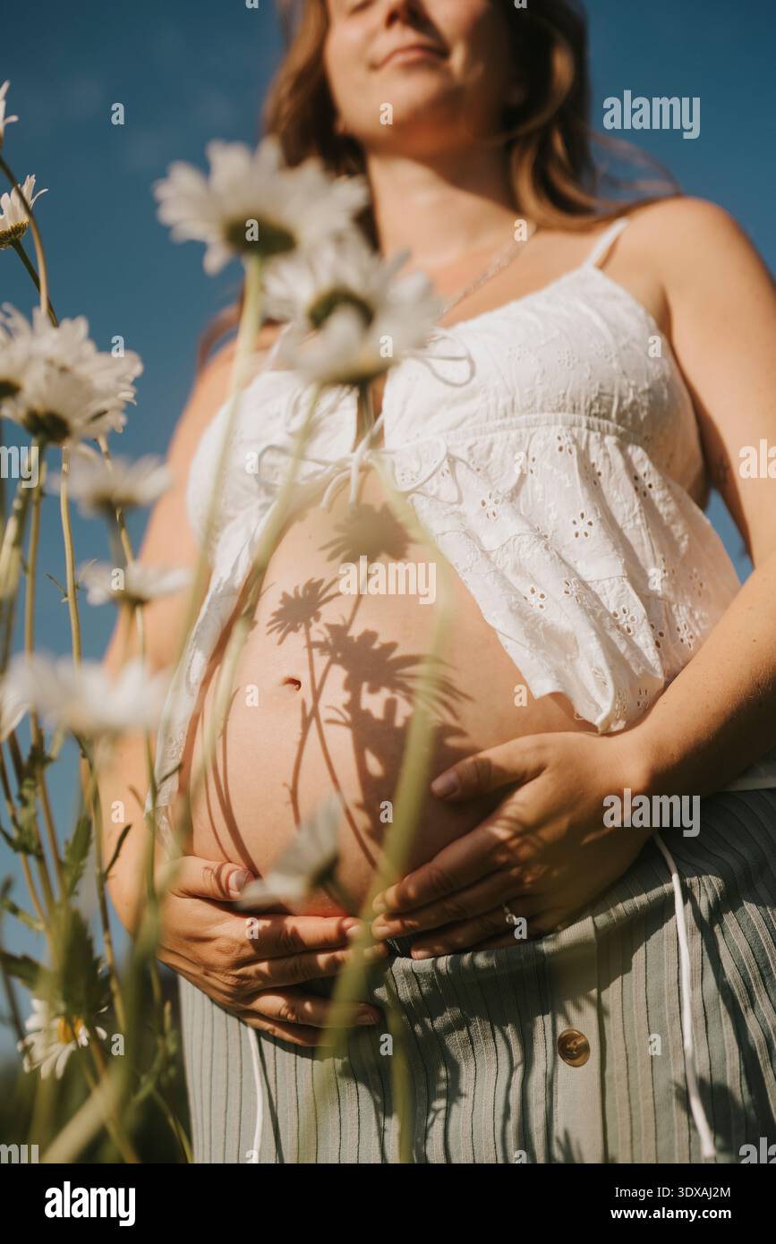Femme enceinte touchant le ventre tout en se tenant debout au milieu des fleurs dans le champ Banque D'Images