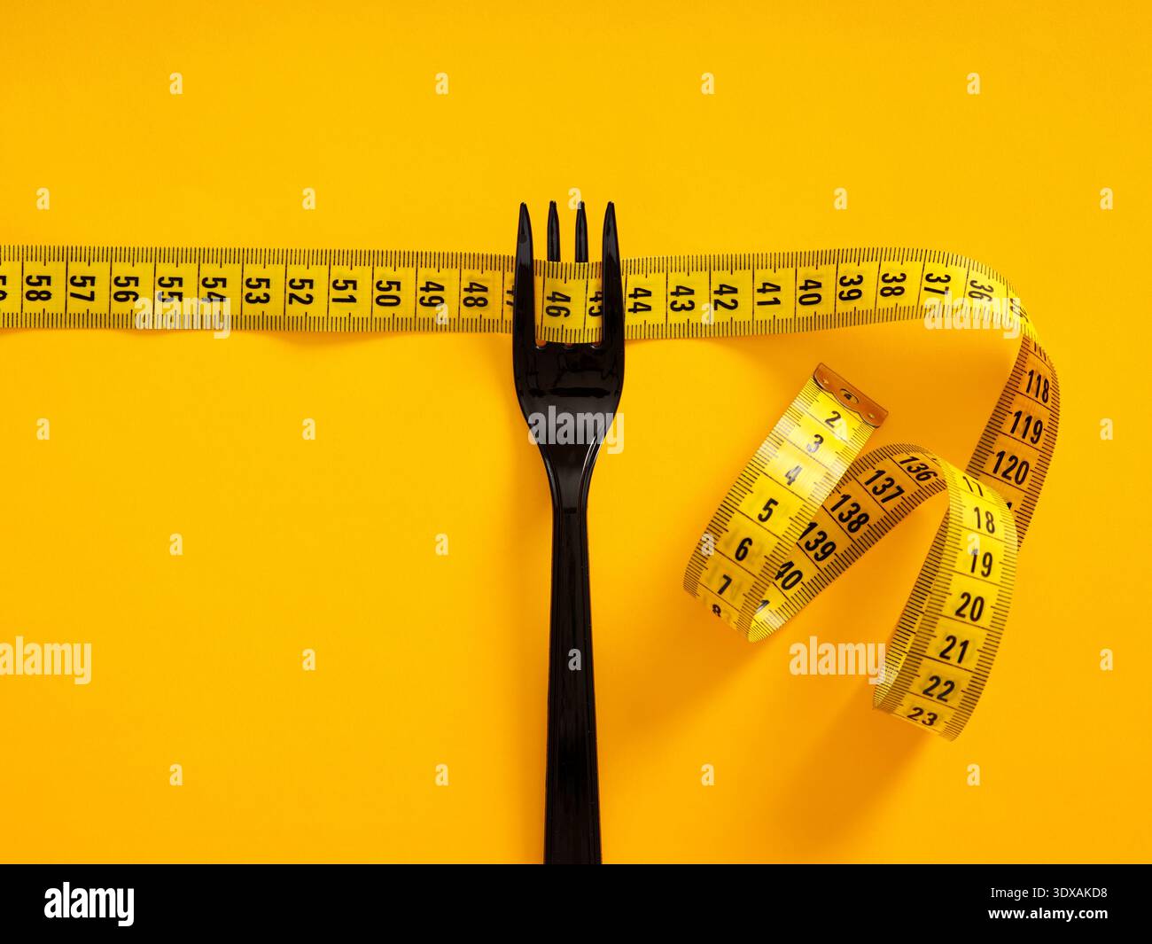 Fourchette noire et ruban à mesurer jaune sur fond jaune, symbolisant une alimentation saine, le contrôle des portions et les objectifs de forme physique Banque D'Images