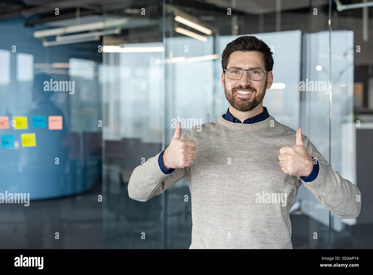 Homme souriant dans un cadre de bureau donnant deux pouces vers le haut, exprimant le succès, l'approbation, la rétroaction positive, et l'accord dans un environnement d'affaires professionnel Banque D'Images