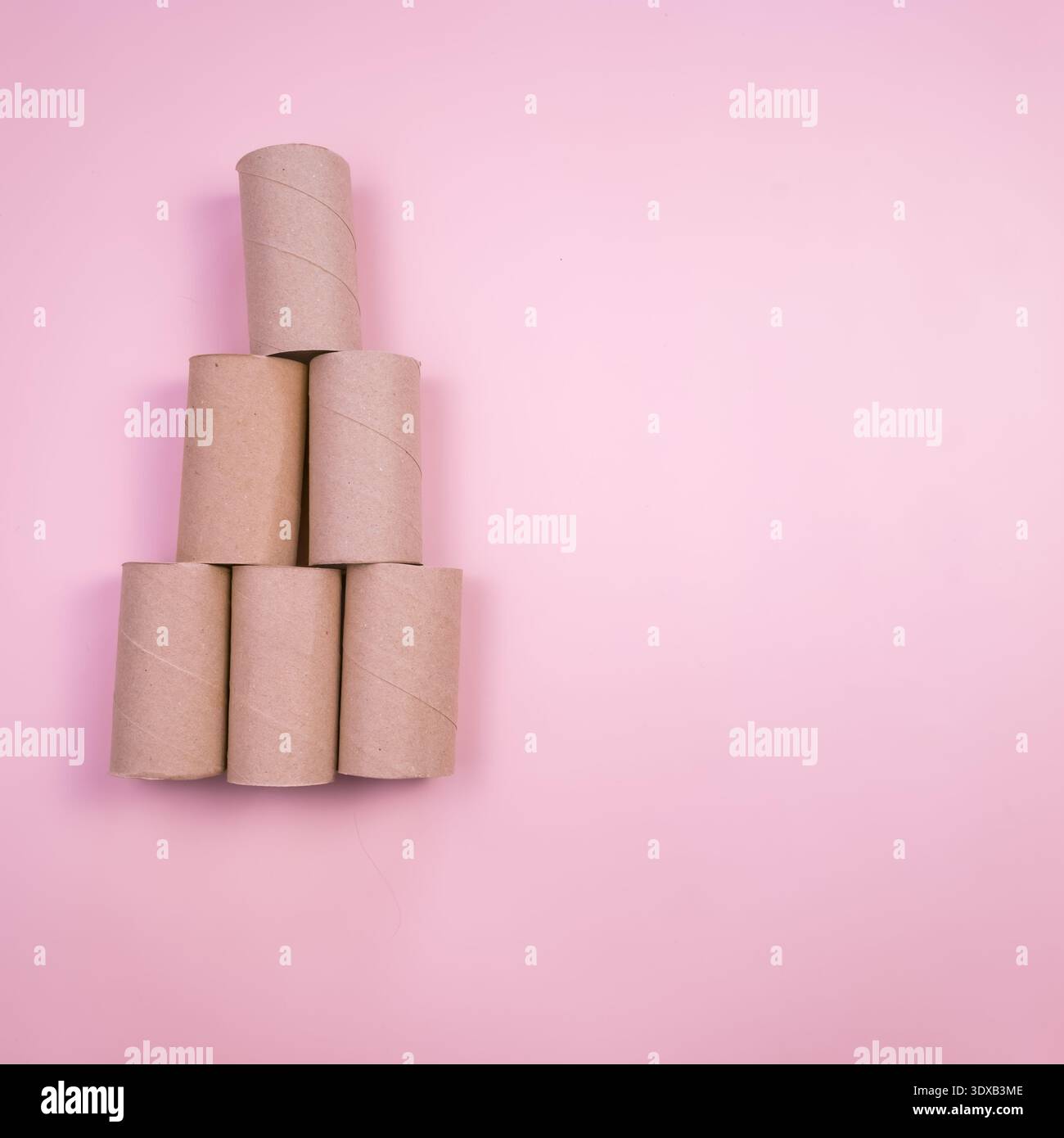 Une pyramide de tubes en carton de papier toilette vides disposés sur un fond rose. Les tubes sont de hauteurs variables et sont empilés selon un format triangulaire Banque D'Images