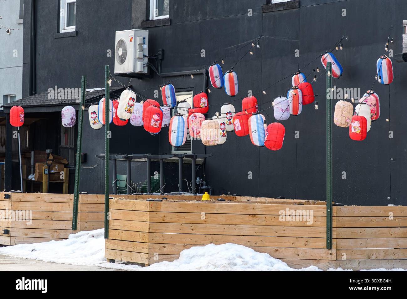 Lanternes en papier rouge et blanc accrochées à des jeux de lumières au-dessus du patio en bois et de la neige. Banque D'Images