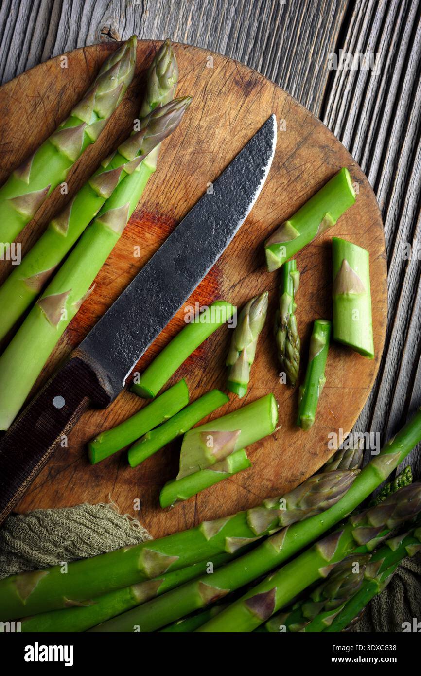 Asperges vertes attachées avec un couteau placé sur une planche à découper ronde en bois légumes biologiques frais. Plat, vue de dessus Banque D'Images