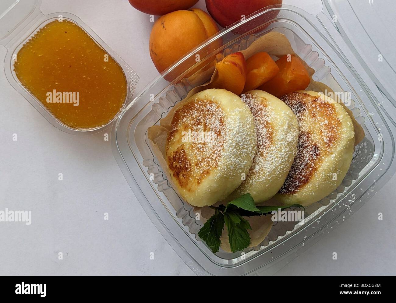Une délicieuse boîte de petit déjeuner avec crêpe de fromage cottage moelleux avec confiture de pêches Syrniki Banque D'Images