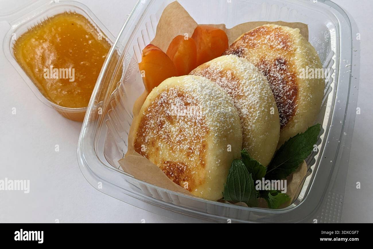 Une délicieuse boîte de petit déjeuner avec crêpe de fromage cottage moelleux avec confiture de pêches Syrniki Banque D'Images