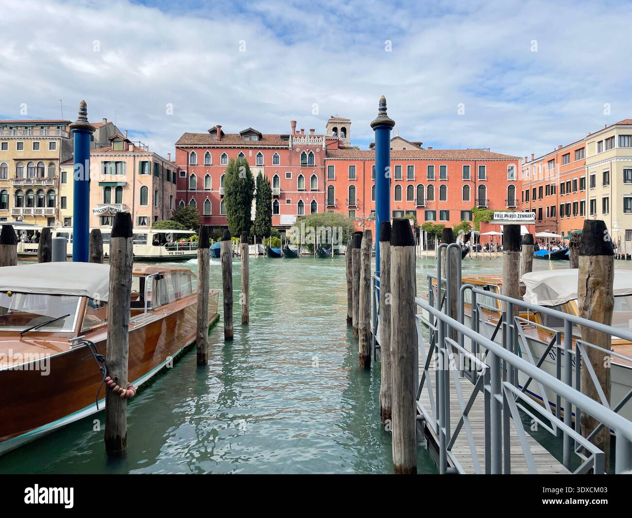 Des bateaux et des postes d'amarrage en bois bordent un canal à Venise tandis que les bâtiments historiques du front de mer réfléchissent sur l'eau. Banque D'Images