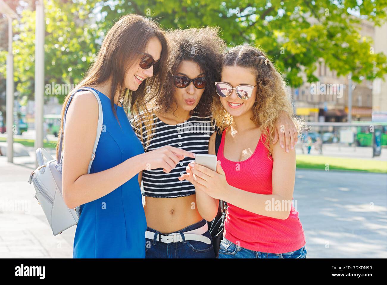Trois amis profitant d'une journée ensoleillée dans le parc tout en regardant un smartphone ensemble Banque D'Images
