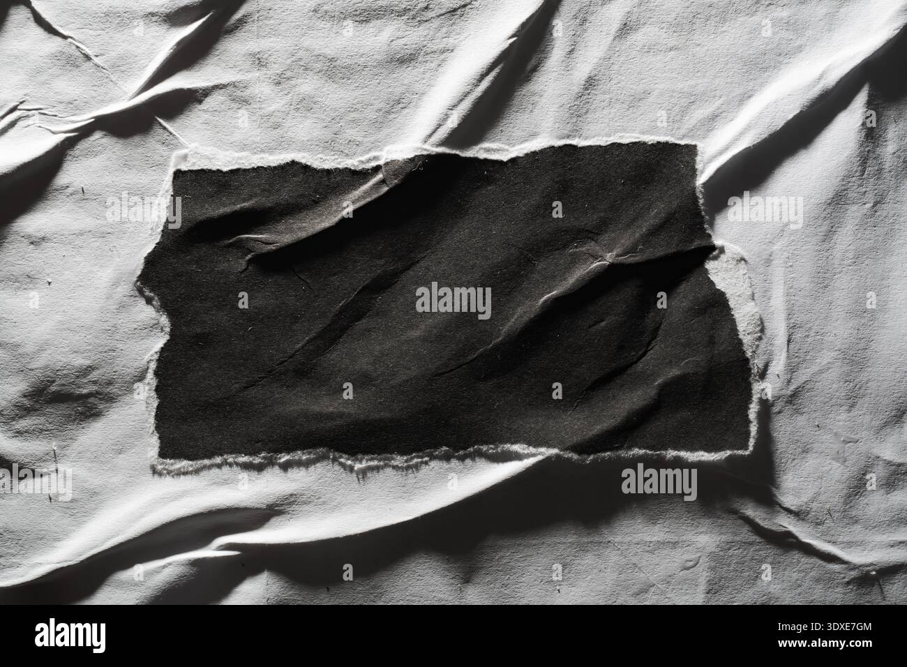 Composition à contraste élevé avec un morceau de papier noir rectangulaire dentelé centré sur une surface de papier blanc fortement froissée et altérée. Banque D'Images