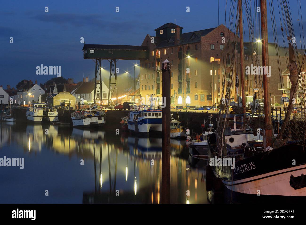 Puits à côté du port de mer, North Norfolk, Grande-Bretagne. Pittoresque côte britannique au crépuscule avec des lumières illuminant les bateaux de pêche, Angleterre. Banque D'Images