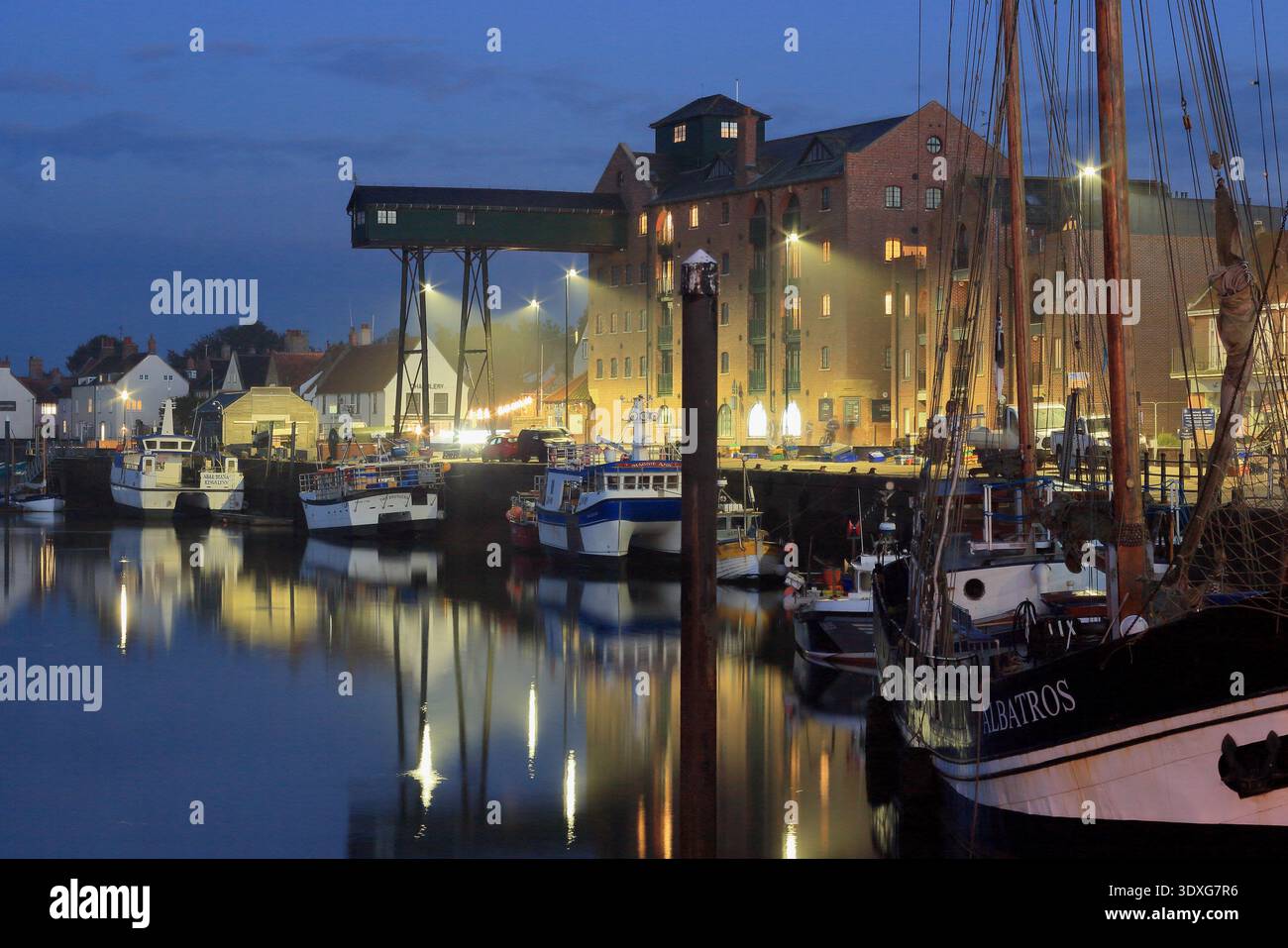 Puits à côté du port de mer, North Norfolk, Grande-Bretagne. Pittoresque côte britannique au crépuscule avec des lumières illuminant les bateaux de pêche, Angleterre. Banque D'Images