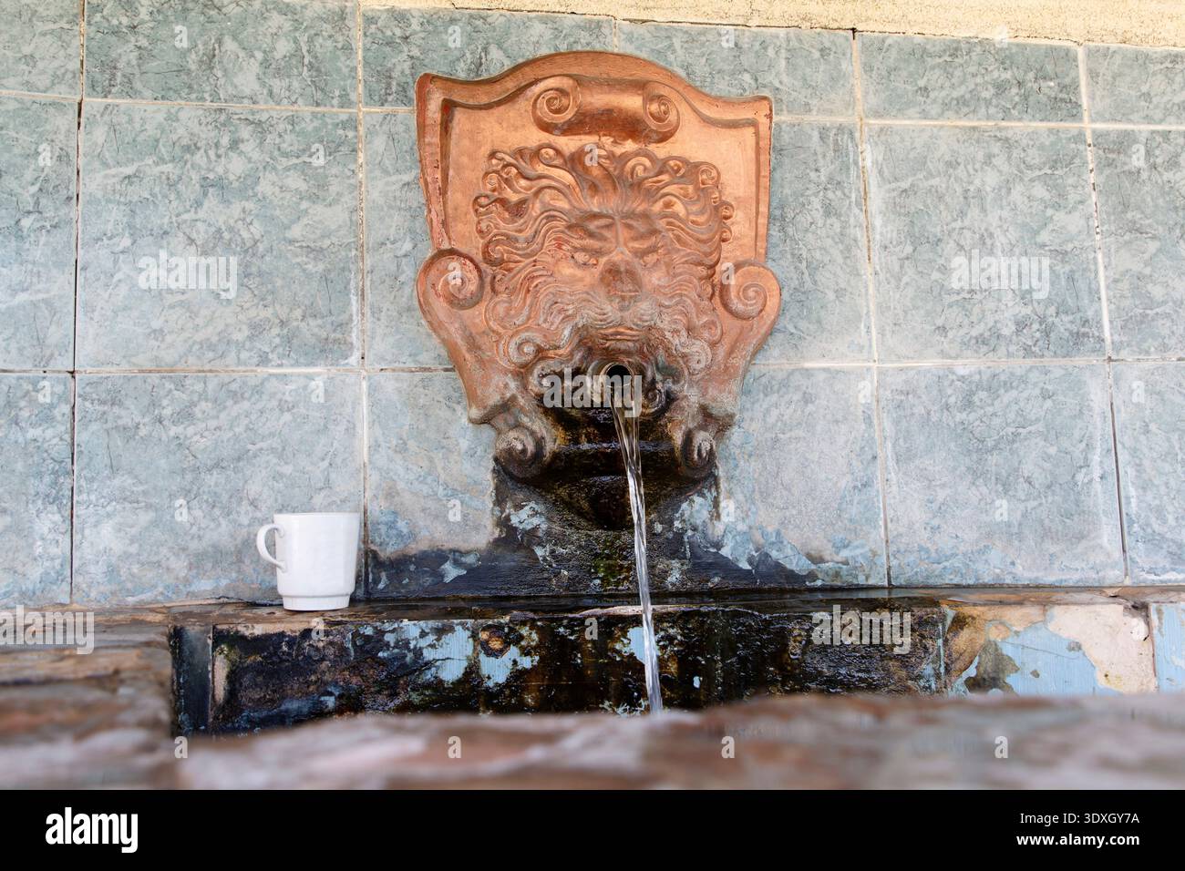 Ancienne fontaine publique ornée d'une sculpture ornée d'une tête de lion. L'eau douce de source coule dans un bassin altéré. Scène rustique avec vieilli bleu-gris t Banque D'Images