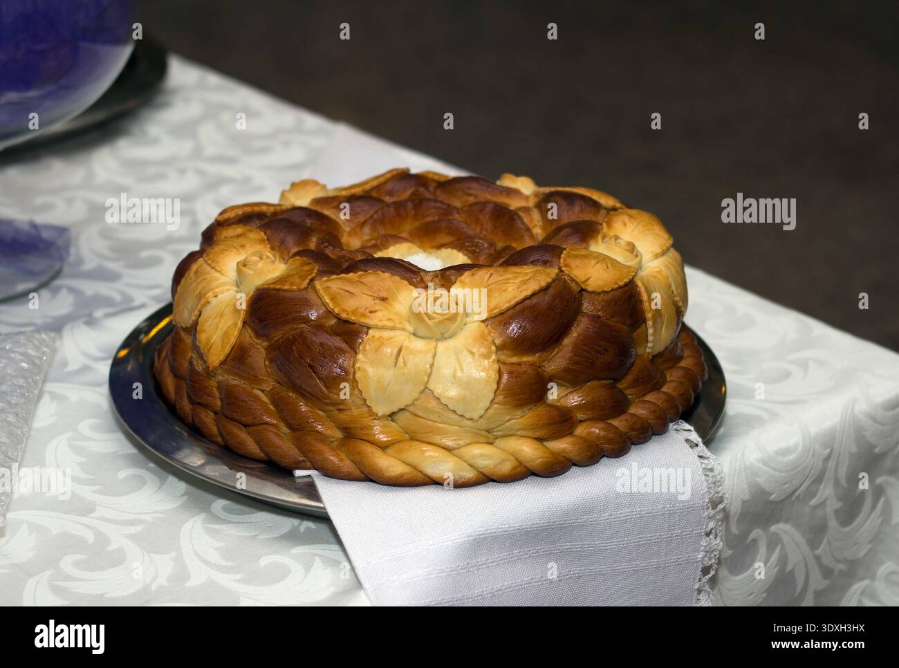 Pain de fête traditionnel. La croûte tressée brun doré est décorée de fleurs et servie sur un plateau argenté sur une nappe blanche Banque D'Images