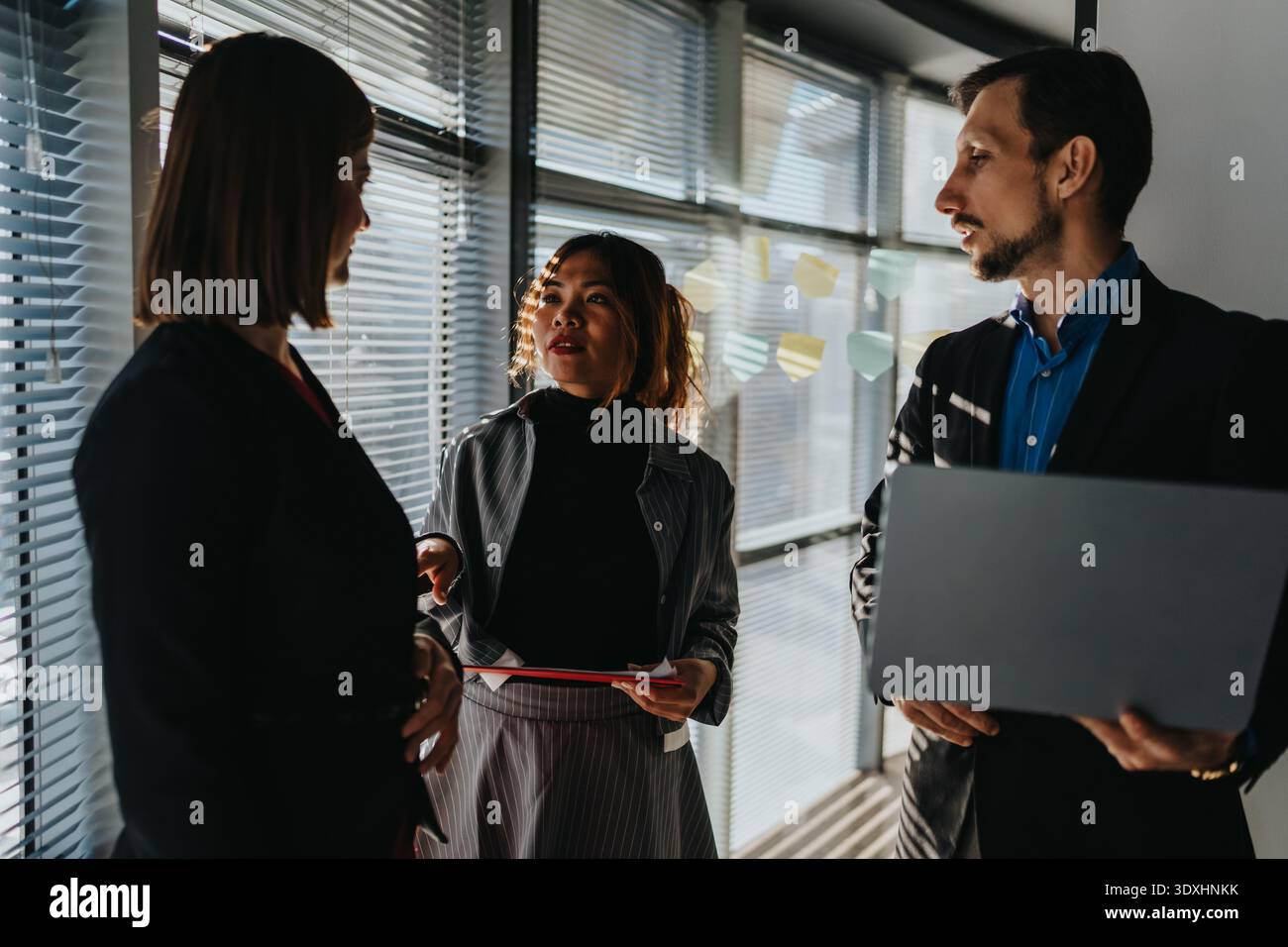 Trois professionnels discutent des idées de projet dans un bureau moderne près d'une fenêtre avec des notes adhésives Banque D'Images