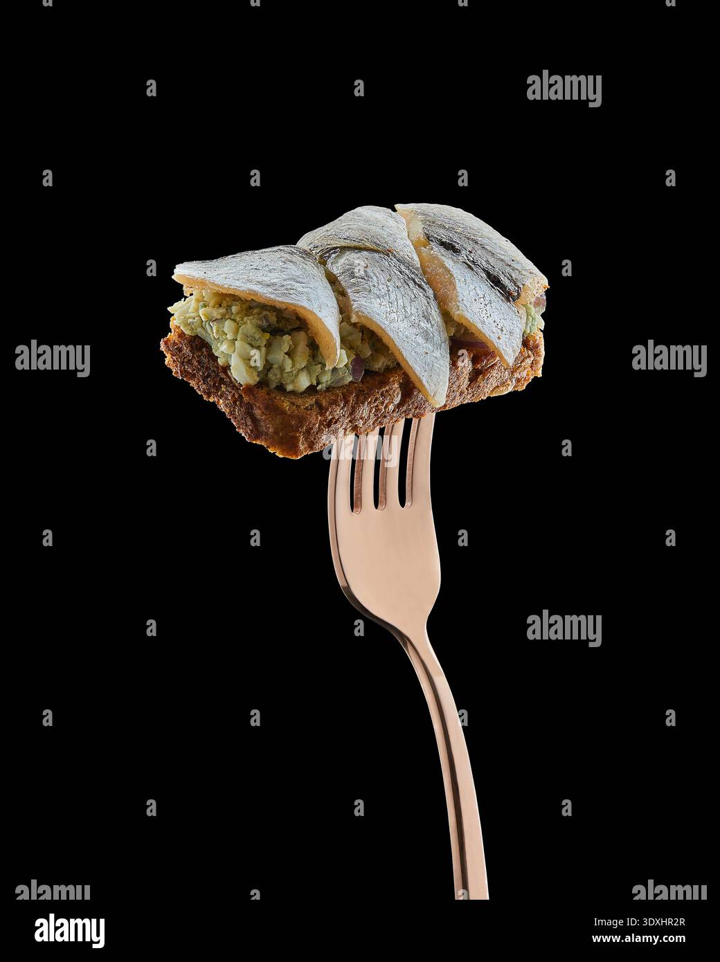 Sandwich sprat ouvert avec pain de seigle, salade d'œufs et poisson équilibré sur fourchette isolé sur fond noir. Banque D'Images