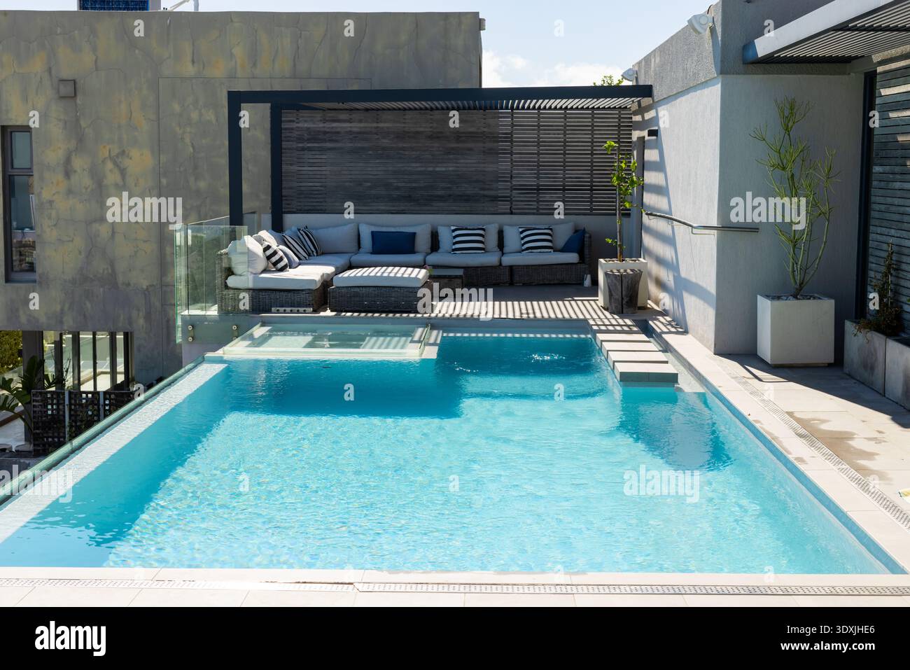 Piscine rectangulaire turquoise scintille sur le toit-terrasse avec ombres pergola et canapé en osier Banque D'Images