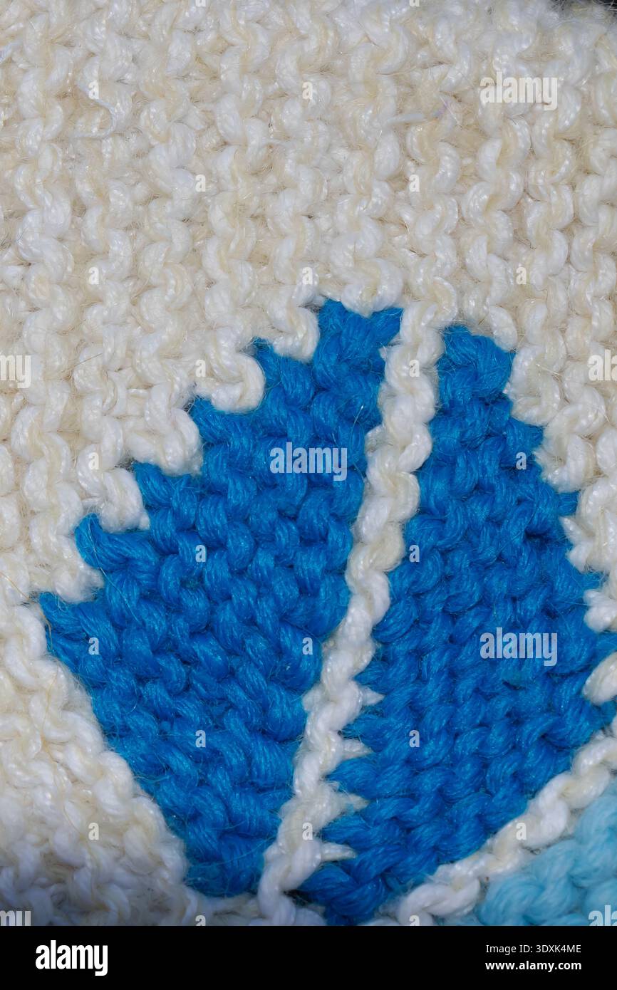 Vue macro d'un motif de feuille bleue tricoté dans un tissu de laine blanche, soulignant la texture détaillée du fil, l'artisanat fait à la main et le desi textile décoratif Banque D'Images