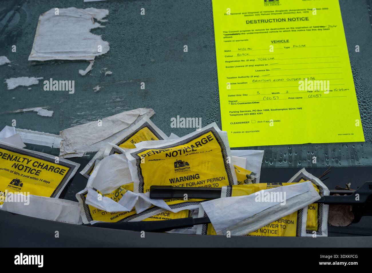 Billets de stationnement, avis de pénalité fixe et avis de déménagement collectés sur le pare-brise d'un véhicule stationné illégalement sur le bord de la route à Southampton. Banque D'Images