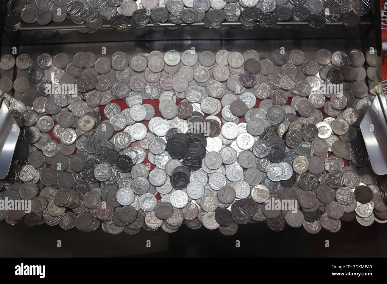 Des douzaines de pièces de monnaie apparaissent suspendues au-dessus de la goutte d'argent d'un poussoir de pièce d'arcade vintage ou d'une machine de jeu en cascade de penny. Banque D'Images