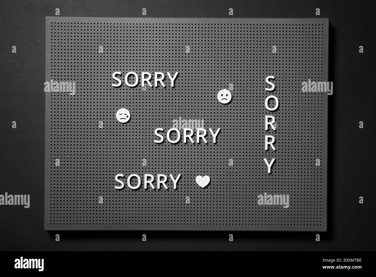 Tableau d'affichage avec des mots DÉSOLÉ, sourires tristes et coeur sur fond sombre Banque D'Images