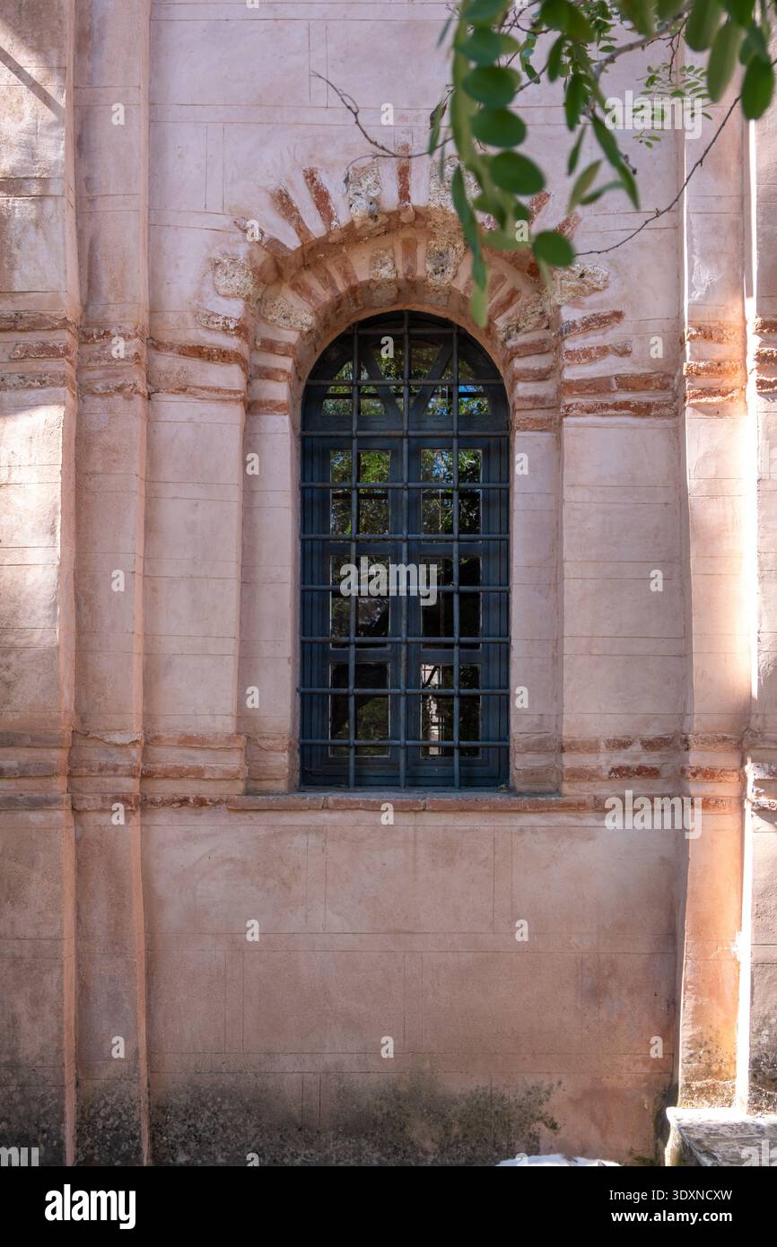 Fenêtre cintrée du monastère avec caillebotis de fer à Nea Moni sur l'île de Chios, Grèce. Cadre en pierre pâle et brique dans des couleurs terreuses chaudes Banque D'Images