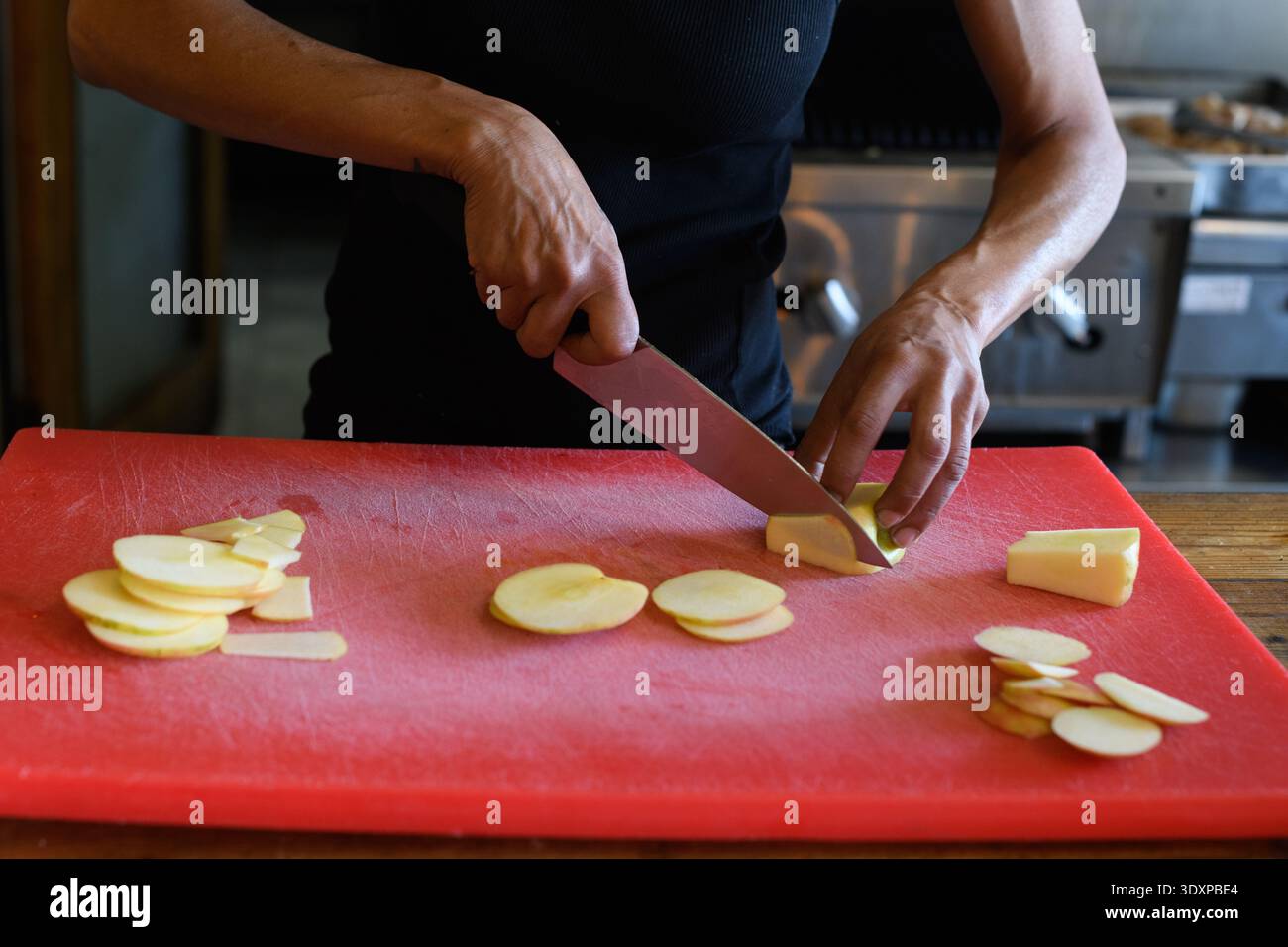 Un chef pâtissier utilise un grand couteau aiguisé pour couper de fines tranches de pomme pour un dessert sucré et cordonnier. Banque D'Images
