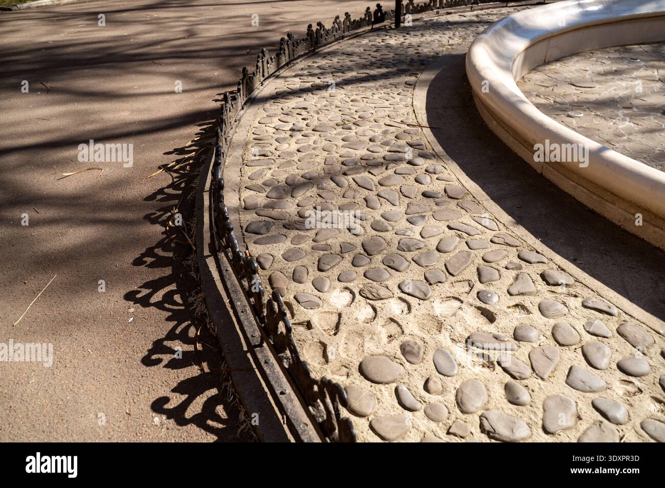 Garde-corps en métal orné projetant une longue ombre artistique sur un trottoir pavé Banque D'Images