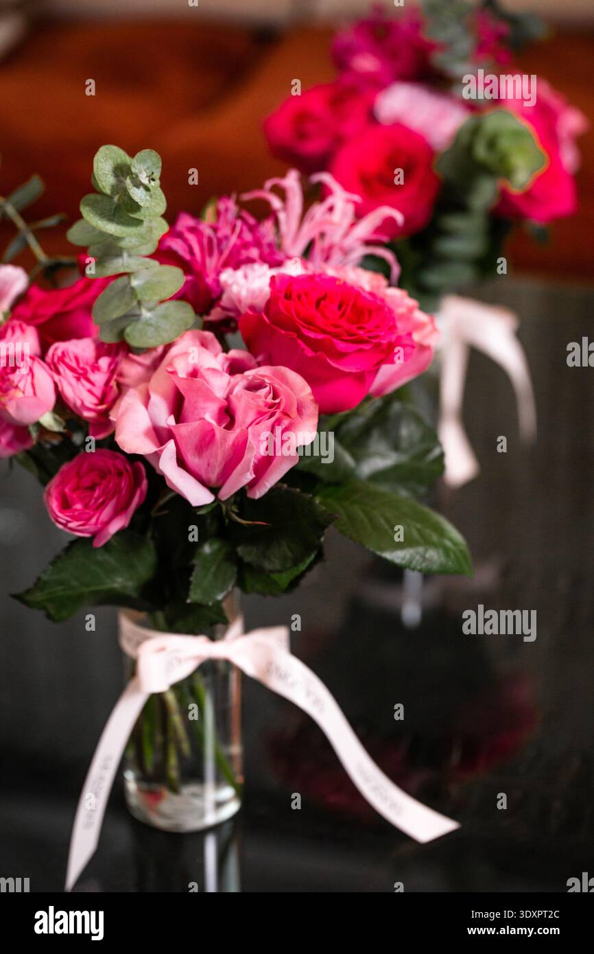 Bouquet rose avec eucalyptus dans un vase en verre sur une surface réfléchissante sombre Banque D'Images